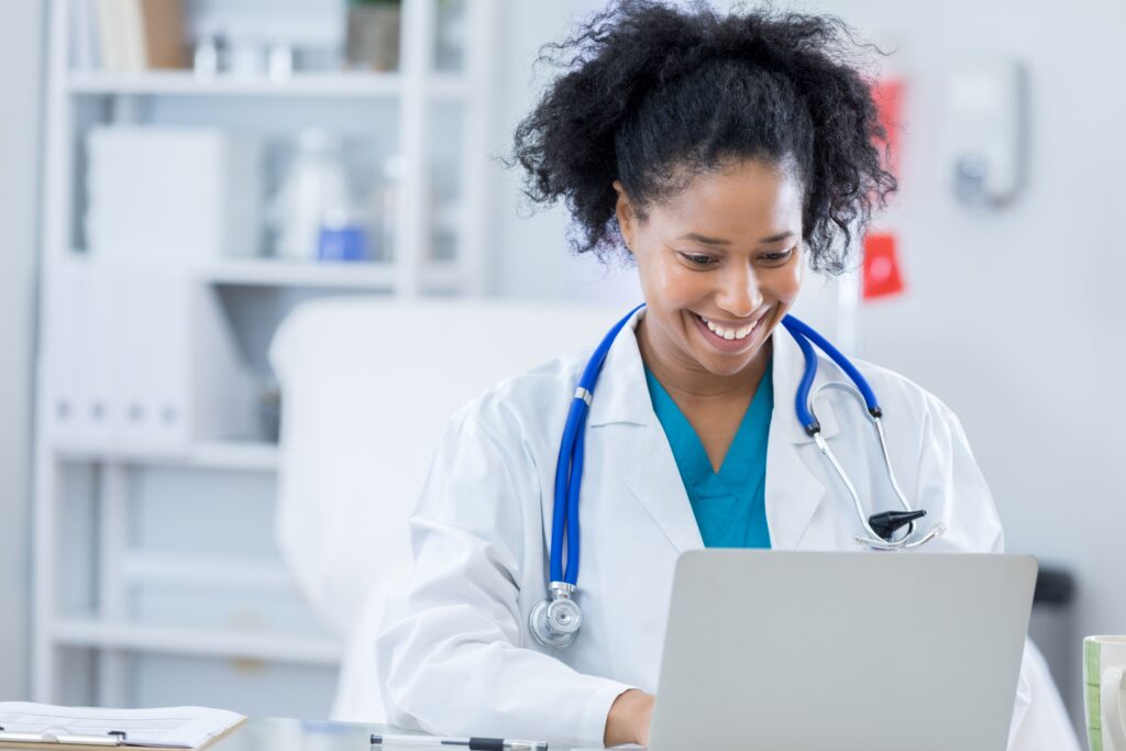 female doctor is smiling and working on a laptop computer